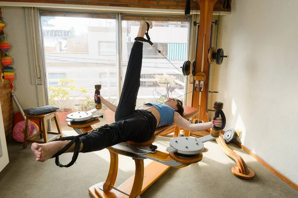 侧视女人仰卧在床上 用滑轮在家里锻炼身体的平衡和力量 同时抬起和放下双腿 — 图库照片