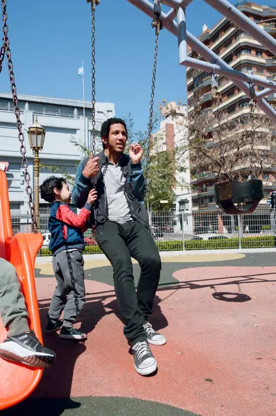 Latin Venezuelan family, happy young child playing with his father on swing in park