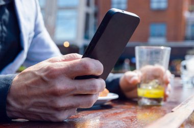 Açık hava restoranında oturan, elinde telefonla mesaj gönderen, kahvaltıda portakal suyu ile sandviç yiyen, uzay fotokopisi çeken...