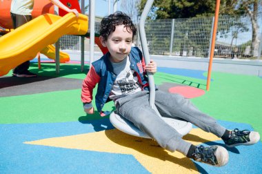 Mutlu ve eğlenceli genç Afro Latin Venezuelalı çocuk oyun bahçesinde oturuyor, öğlen parkta oynuyor, boşluğu kopyalıyor..