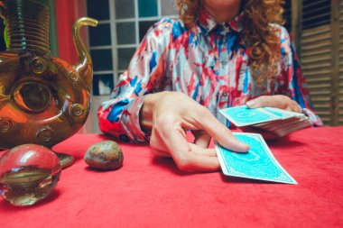 Tanımlanamayan Kafkas tarot okuyucu kadın, evinde oturuyor, güverteden kartı alıyor ve masaya yerleştiriyor, yıldızlarla okumaya başlıyor..