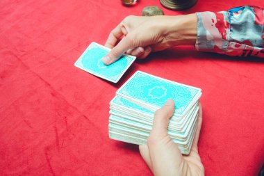 Kafkasyalı bir kadının mavi tarot kartını kırmızı masa örtüsü, tarot konsepti ve fotokopi alanı ile masaya koyması.