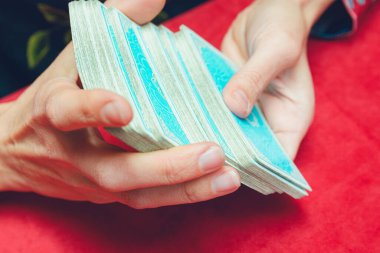 Masada mavi tarot kartlarını kırmızı masa örtüsüyle karıştıran tanınmayan genç beyaz tarot okuyucusunun elleri..