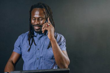 Afrika kökenli genç bir işadamı rastalı, sakallı ve mavi gömlekli, gülümseyen mutlu bir şekilde ayakta duruyor restoranın içinde, ön görüşte, iş adamları kavramında telefonla konuşuyor..