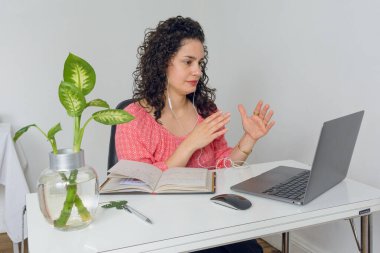 Genç Latin iş kadını ofisinde oturmuş bilgisayarla telefonda konuşuyor kulaklık takıyor, el hareketleri yapıyor, iş ve teknoloji kavramları yapıyor, boşlukları kopyalıyor.