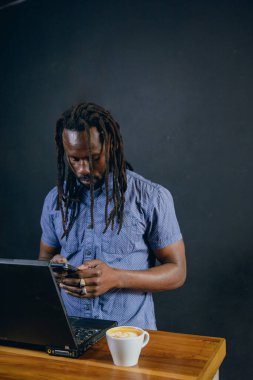 Siyah iş adamı, rastalı, sakallı ve günlük kıyafetleri olan, kafede durmuş, telefon mesajları göndermekle meşgul, kopyalama alanı