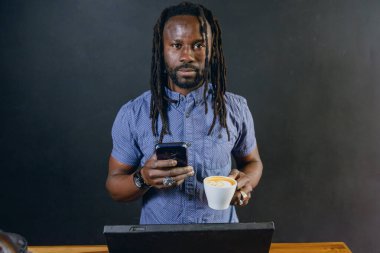 Genç Afrikalı serbest meslek adamının portresi. Restoranda dizüstü bilgisayarıyla çalışıyor. Kahve içiyor ve kameraya bakıyor.