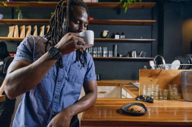 Siyah saçlı, sakallı ve günlük kıyafetleri olan bir adam restoranda ayakta durup tezgahta durup içen ve kahvaltıda kahvenin tadını çıkaran bir müşteri. yaşam tarzı kavramı, kopyalama alanı