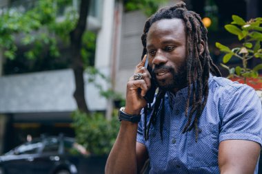 Rastalı ve sakallı Afrikalı bir adamın yakın çekimi, açık havada oturup, telefon görüşmesi, teknoloji ve yaşam tarzı konsepti hakkında konuşmak, kopyalama alanı..