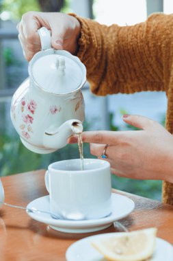 Beyaz porselen çaydanlığıyla beyaz porselen bardağa sıcak çay döken beyaz porselen bardaktaki tanınmamış beyaz kadının elleri.