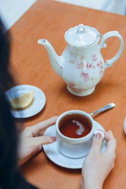 Masanın üzerinde elinde porselen bardakla çay içen tanınmayan bir kadının yakın çekim görüntüsü. Boşluğu kopyala.