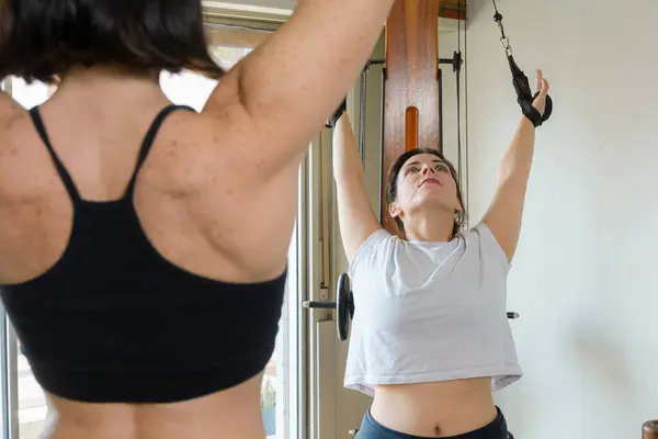 Caucasian adult woman trainer standing working in stretching class with her student at home showing her what exercises and body movements are like.