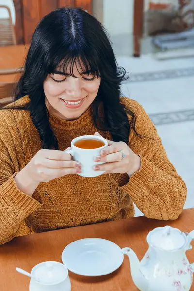 top view of beautiful latin young woman sitting drinking tea holding white porcelain cup with her hands. She is happy smiling and enjoying day.