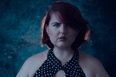 Ön manzara, stüdyo portresi. Kırmızı saçlı, beyaz noktalı mavi elbiseli ve kameraya bakan Latin bir kadın..