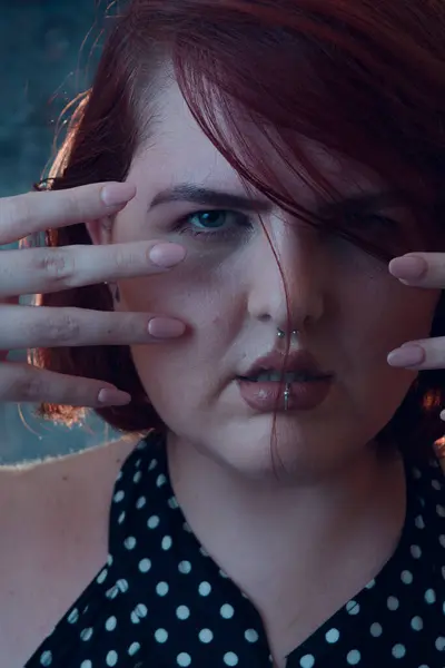 Close-up vertical portrait of young Latina of Argentinian ethnicity, plus size, with short red hair, posing with hands on face