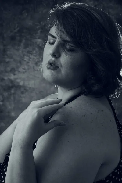 artistic black and white vertical portrait of overweight young woman standing in profile with eyes closed posing with hands on shoulder