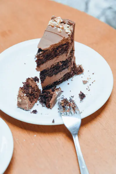 Tabakta çatalla, ahşap masada kesilmiş çikolatalı kekin dikey görüntüsü, boşluğu kopyala