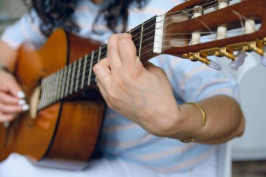 Tanımlanamayan beyaz bir kadının evinde akustik gitar çalması, şarkılar çalması, boyun akoruna odaklanması.