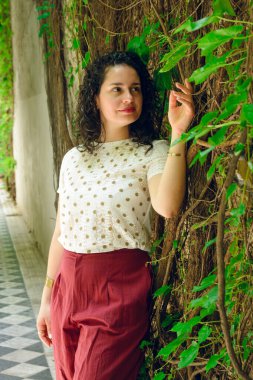 dikey portre genç latin venezuelalı iş kadını, evinde duvara yaslanmış, dinleniyor bitkileri, insanları izliyor, uzayı kopyalıyor..