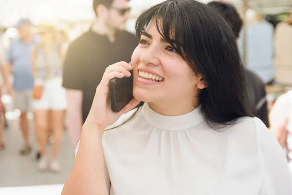 young latin woman smiling happy talking on phone on call, while walking around fair and looking at clothes on stands, people and technology concept, copy space.