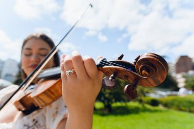 Açık havada keman çalan bulanık Latin müzisyen kadının geniş açılı görüntüsü, keman boynuna odaklan ve arka planda açık gökyüzü olan deniz kabuğu ve boşluğu kopyala.