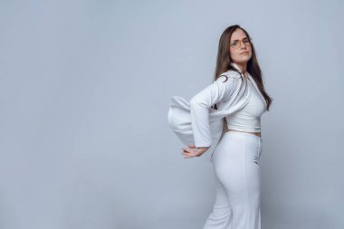 Gözlüklü ve uzun saçlı genç Latin kadın kameraya bakarak mutlu poz veriyor, beyaz resmi giyiniyor, beyaz arka planda çekim yapıyor ve fotokopi çekiyor.