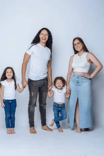 stock image young latin family of father mother and two young girls daughters, having fun posing and smiling, with pants and white flannel, studio shot, white background.