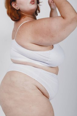 Beyaz arka planda beyaz iç çamaşırlı, selülitli, tanımlanamayan beyaz tenli, beyaz bir kadının yakın çekimi.