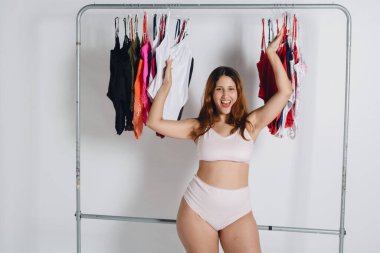 young latin argentinian woman in underwear, standing laughing and posing with rack with underwear behind her, studio shot with white background. clipart