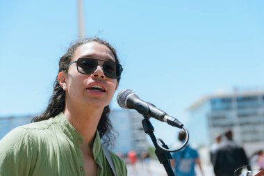 Venezuelalı genç Latin kökenli, uzun saçlı, koyu gözlülü, sokak ortasında Arjantin 'in Puerto Madero semtinde gösteri yapan sokak müzisyeninin portresi.