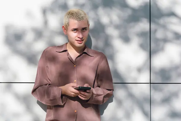 Jeune Homme Aux Cheveux Blonds Tient Devant Mur Tenant Téléphone Images De Stock Libres De Droits