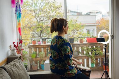 Tanımlanamayan Yetişkin Kadın 'ın çevrimiçi davul dersinde telefondaki görüntüsü. O bir Djembe davulu çalıyor ve telefon bir ışık yüzüğüyle tripodun üzerinde.