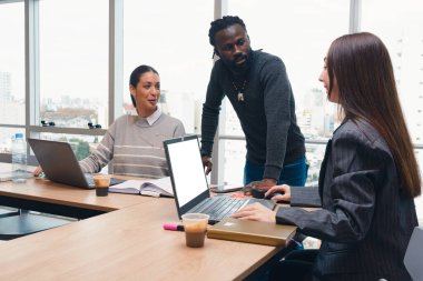 Üç genç insan dizüstü bilgisayarları ve bir kitapla oturmuş kendi aralarında bir iş hakkında tartışıyorlar. Bir adam dizüstü bilgisayarı kullanan kadına bakıyor. Sahne profesyonel ve odaklı.
