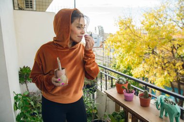 Balkon bahçesindeki genç kadın bitkilerinin kokusunu yalıyor ve tadını çıkarıyor. Sahne saksı bitkileri ve bankla dolu bir balkonda geçiyor. Kadın manzaranın ve bitkilerin tadını çıkarıyor.