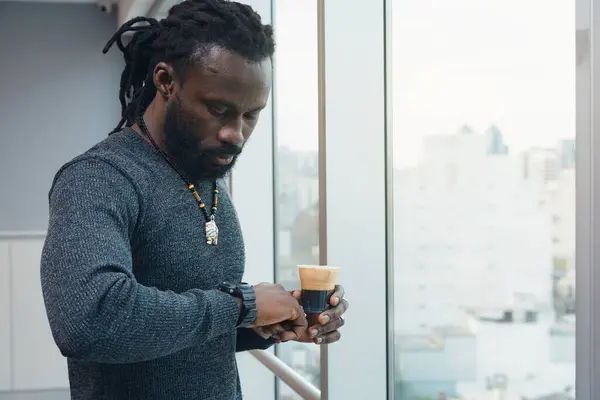 Stock image African Entrepreneur Man with dreadlocks in co-working space is checking time on clock to finish work. concept of entrepreneurial and business people, as the man is enjoying his coffee while wait.