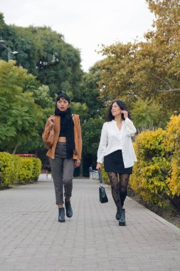 Parkta yürüyen iki Latin kadın üniversiteden ayrılıp evlerine dönüyorlar, dikey görüntü, dikey görüntü, sağa bakarken eğleniyorlar. Sosyal medya için yaşam tarzı kavramı.