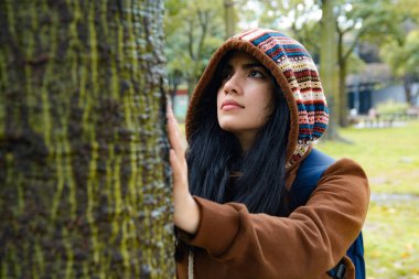 Huzur ve hayranlık ifadesiyle mutlu genç kadın elleriyle ağaca dokunuyor ve havlayarak sükuneti hissediyor. Parkta durmuş, doğayla bağ kuruyor..