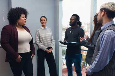 Yönetim kurulunda toplanan çok ırklı ve çok ırklı bir grup insan, pencere kenarında dikilip sohbet ediyorlar, Afro 'yla birlikte iş konularını açıklayan bir kadın var..