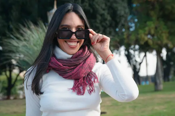 stock image portrait of young woman looking at camera over edge of her glasses, she is in park in city of Buenos Aires, she is happy and smiling