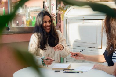 Latin kökenli genç bir kadın çalışma saatlerinde eşiyle dalga geçiyor, balkonda oturuyorlar, sanat okuyorlar, kalemleri boyuyorlar ve masaya kitap çiziyorlar..