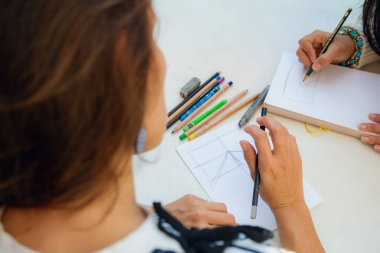 Üst manzara, masanın üzerine çizim yapan tanınmayan bir kadın perspektifi elinde bir grafit kalem, masada renkli kalemler, sınıf konsepti var.