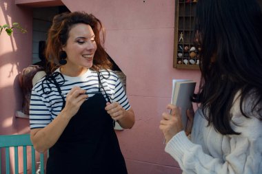 Yetişkin kadınlar evde terapi atölyesinde beraberler, ayakta duruyorlar ve bir tanesi elinde bir kağıt tutarak partnerinin kalemini tutuyor ve bakıp gülümsüyor.