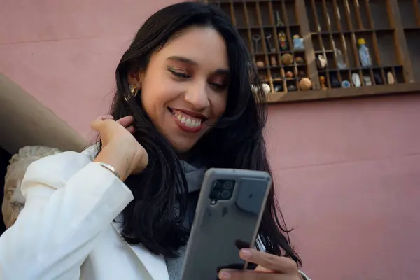 stock image Happy woman in love is smiling at the messages received on her phone, she is combing her hair with her hand and has a mischievous and happy expression, she is holding her phone with her hand, close-up