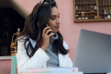Genç Esmer Latin Girişimci Kadın, Arjantinli etnik kökenli, bir telefon görüşmesi için merkez ofiste çalışıyor, müşterilerine hizmet veriyor ve hizmetlerini internet üzerinden dizüstü bilgisayarıyla satıyor. İş konsepti