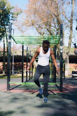 Sosyal medyayı eğitmek için dikey görüntü, adam parkta ip atlıyor, jimnastik eğitim çubuklarının, egzersiz ve sağlıklı yaşam konseptinin yanında duruyor, boşluğu kopyalıyor.