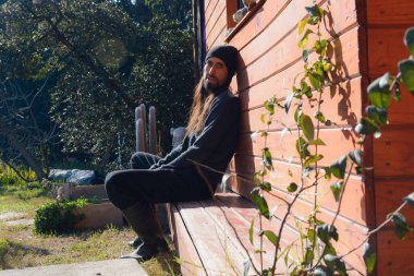 Genç Arjantinli adam, evde oturup duvara yaslanıyor, çalışmaktan yorulmuş, kameraya bakıyor, soğuk, insan ve çiftlik konsepti için kıyafetler giyiyor, mekanı kopyalıyor.