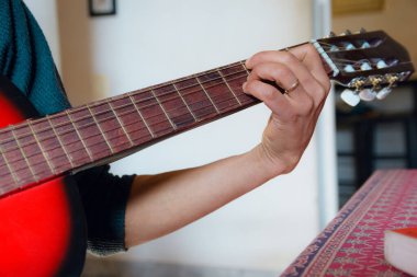 Evde oturan, klasik akustik gitar, kırmızı ahşap gitar, müzik aletleri konsepti, kopyalama mekanı akoru yapan tanınmamış bir adamın erkek eli..