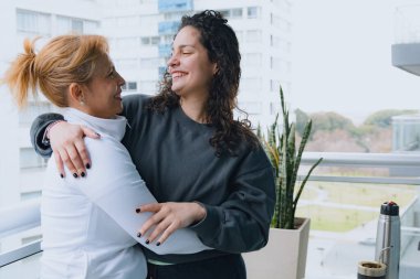 İki Latin kadın birbirine sarılıyor ve anne ile yetişkin kızı arasında sevgi gösteriyor. Otelin balkonunda tatilin tadını çıkarıyorlar..