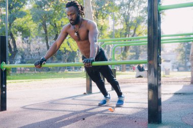 Arm and Man muscle strengthening and growth exercise, black man doing flexion and elbow extension exercise on calisthenics bars in the park clipart