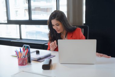Kırmızı elbiseli genç girişimci Latin kadın çalışma alanında çalışıyor, dizüstü bilgisayarla ve defterle oturuyor, insanlar ve iş konsepti, kopyalama alanı.